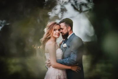 Un abbraccio di Fabrizio e Valeria incorniciato dalle foglie sfocate.